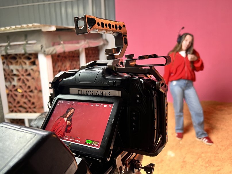 Camera monitor framing a performer in a red jacket against a hot pink wall