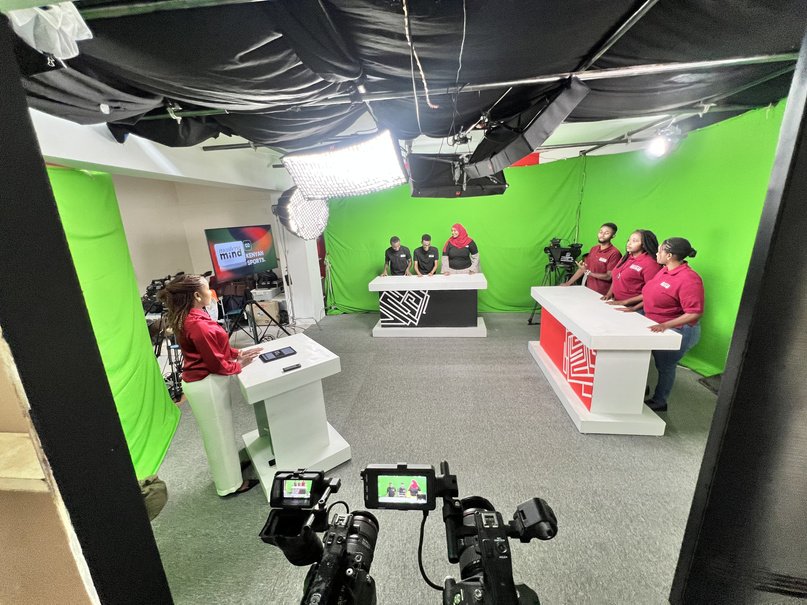 Green-screen television studio with presenters in red at white desks